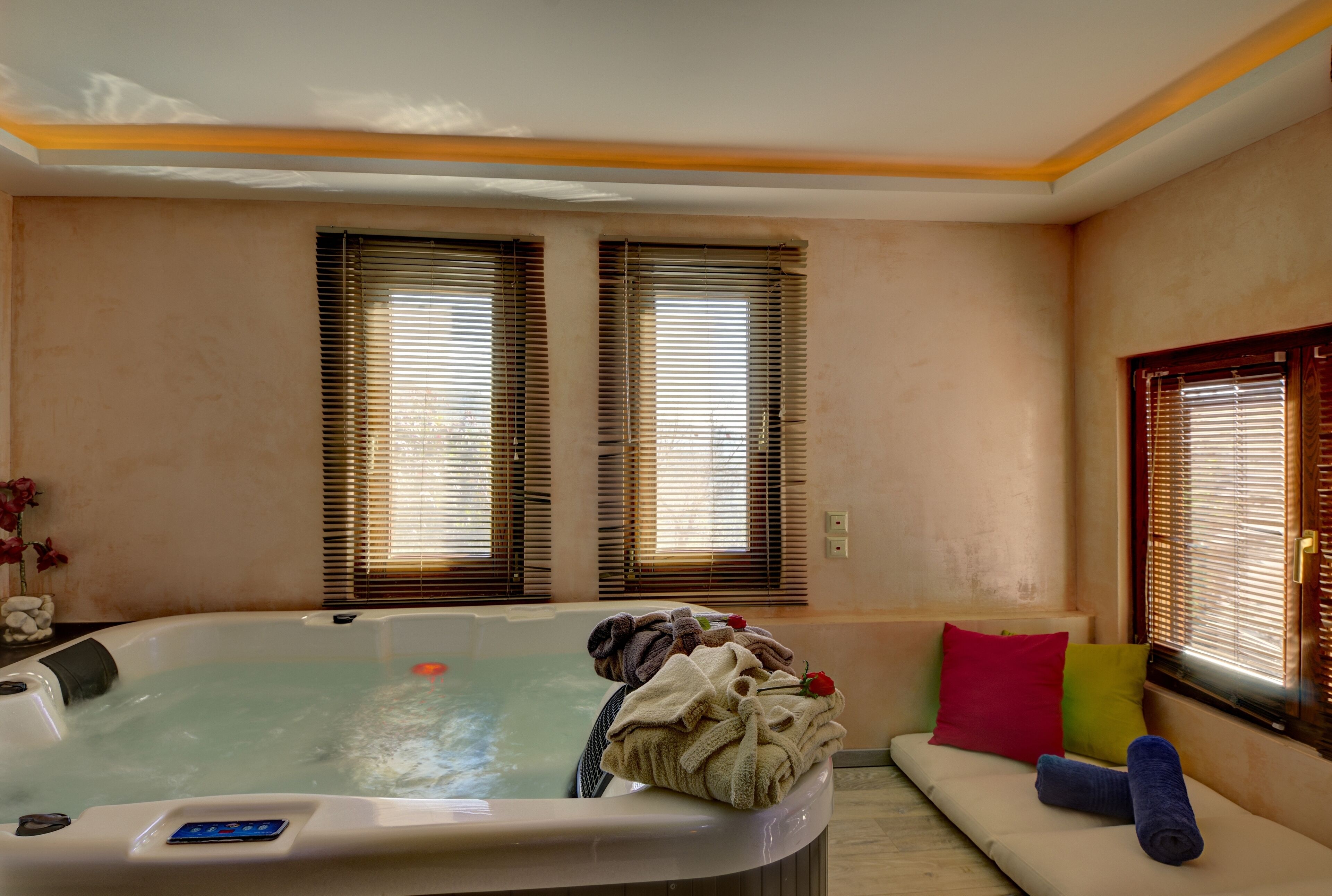 Un cuarto de spa con un jacuzzi, un sofá con cojines de colores y una ventana con persianas.