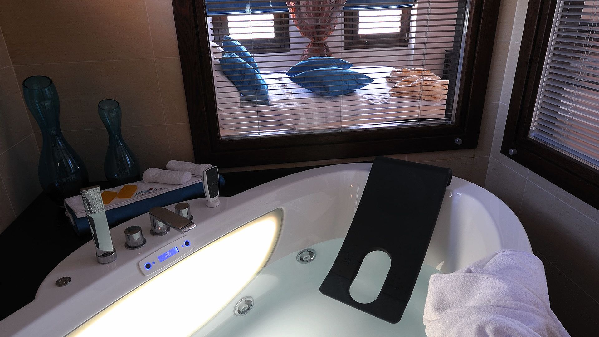 Un baño moderno con una bañera grande, un tocador con espejo y una ventana con persianas.