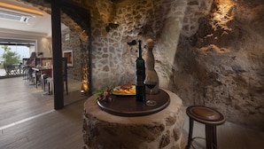 A rustic stone wall interior with a wooden table set for dining, a bottle of wine, and a glass on the table. - Iakovakis Suites & Spa (South Pelion)