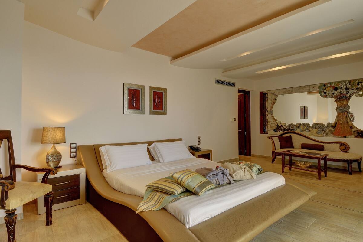 A well-lit bedroom with a large bed, bedside tables, a chair, and a sofa.