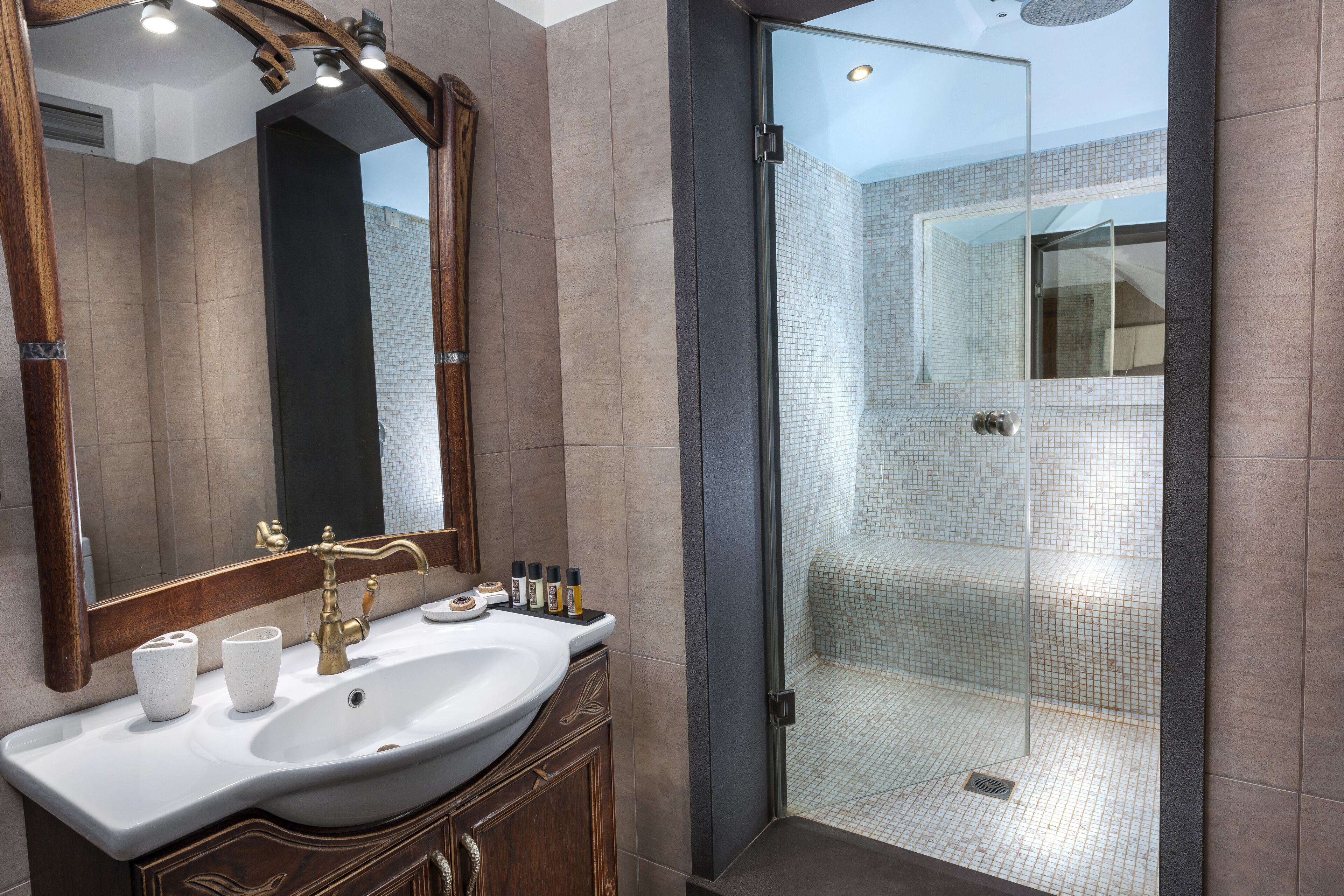 Un baño moderno con un espejo grande, un lavamanos blanco y una zona de ducha con mampara de vidrio.