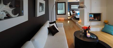 A modern living room with a white sofa, a round coffee table with candles, and a fireplace.
