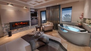 A modern living room with a fireplace, a sofa, a chair, a large bathtub, and a view of a building through the window. - Iakovakis Suites & Spa (South Pelion)