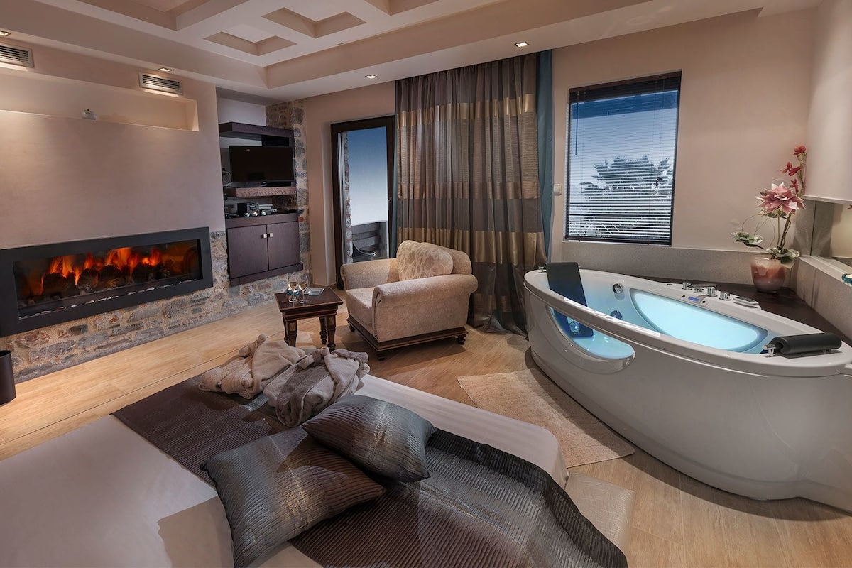 A modern living room with a fireplace, a sofa, a chair, a large bathtub, and a view of a building through the window.