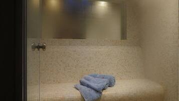 A glass-enclosed room with a bench, a towel, and a ceiling light fixture.