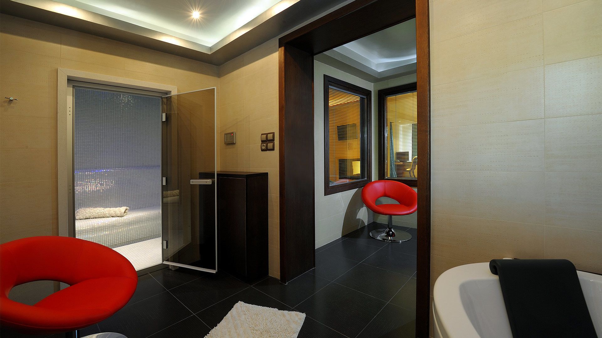 A modern bathroom with a glass shower enclosure, a red chair, and a white toilet.