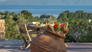 An outdoor dining area with a view of the sea and mountains, featuring rustic wooden furniture and a large vase with flowers. - Iakovakis Suites & Spa (South Pelion)