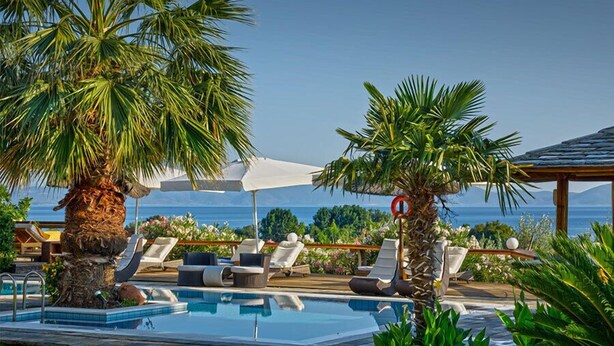 A poolside area with lounge chairs, umbrellas, and a view of the ocean. - Iakovakis Suites & Spa (South Pelion)