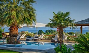 A poolside area with lounge chairs, umbrellas, and a view of the ocean. - Iakovakis Suites & Spa (South Pelion)