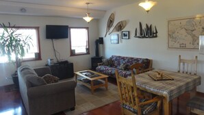 A living room with a sofa, a coffee table, a dining table with chairs, a television, a map on the wall, and a plant. - Smithers Guesthouse (Smithers)