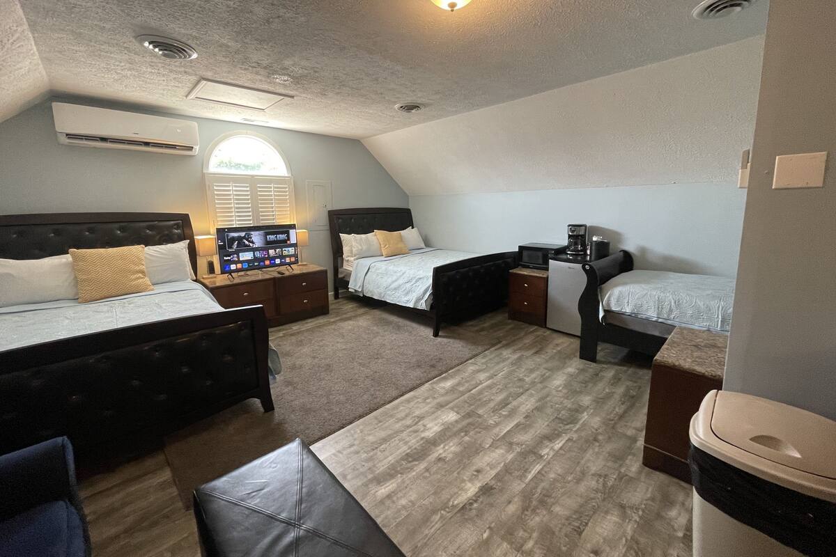 A hotel room with two beds, a desk with a computer, a coffee maker, and a TV displaying a movie.