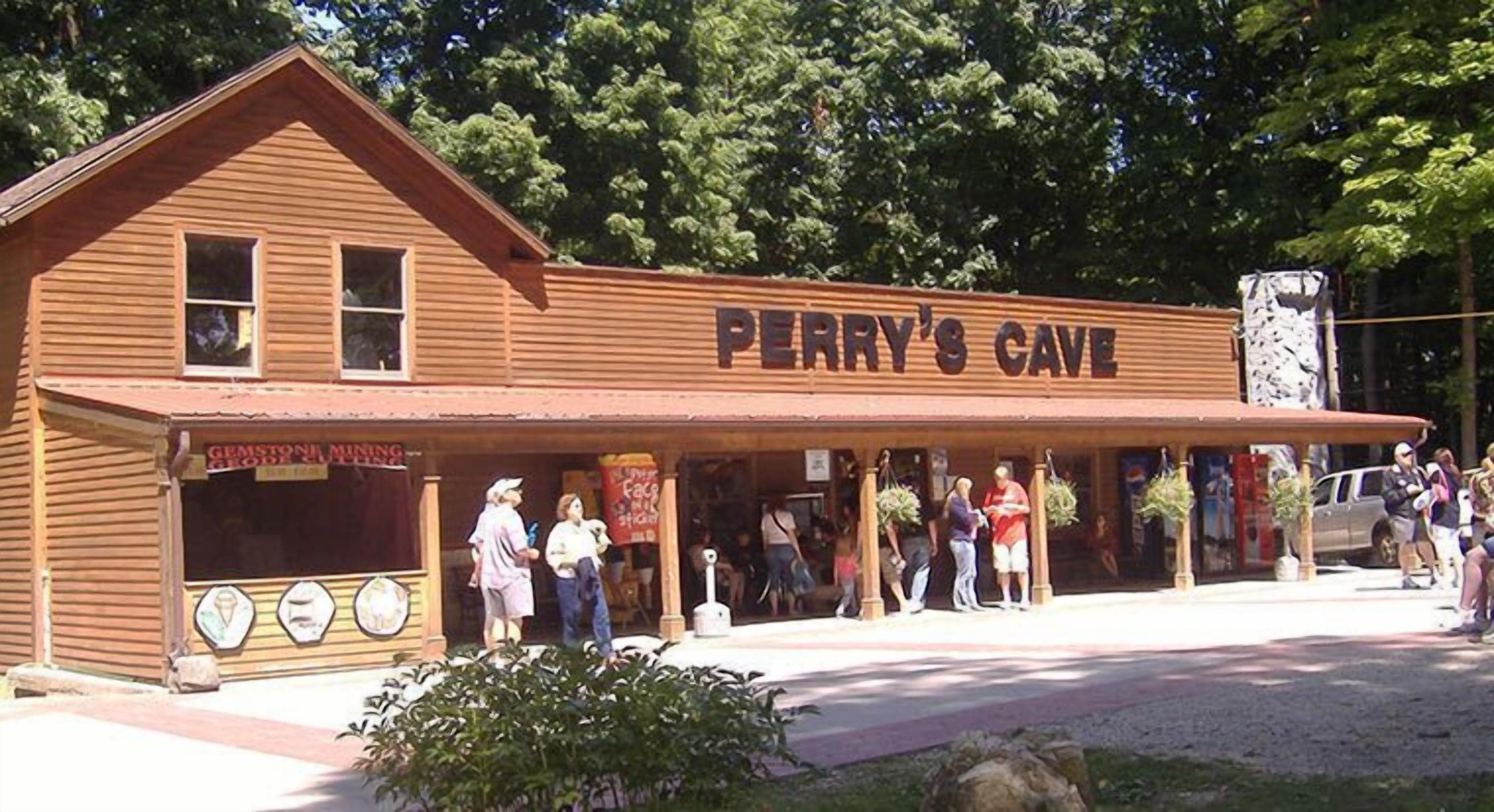 Ein hölzernes Gebäude mit der Aufschrift "Perry's Cave“ und einem überdachten Eingangsbereich sowie einem Schild für "Gemstone Mining Group“.