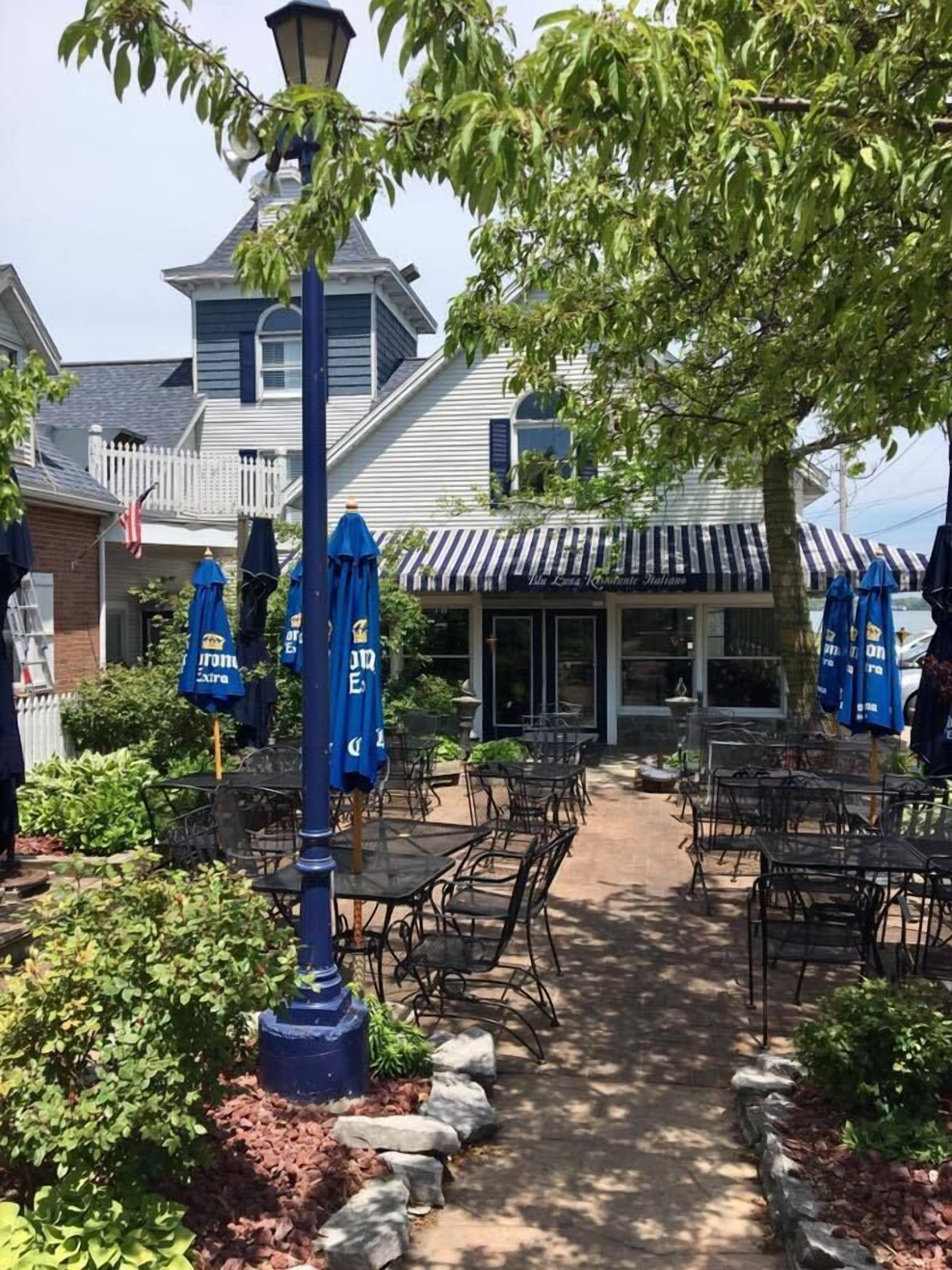 An outdoor seating area with tables and chairs, a blue street lamp, and a building with a striped awning in the background.