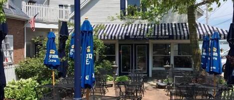 An outdoor seating area with tables and chairs, a blue street lamp, and a building with a striped awning in the background.