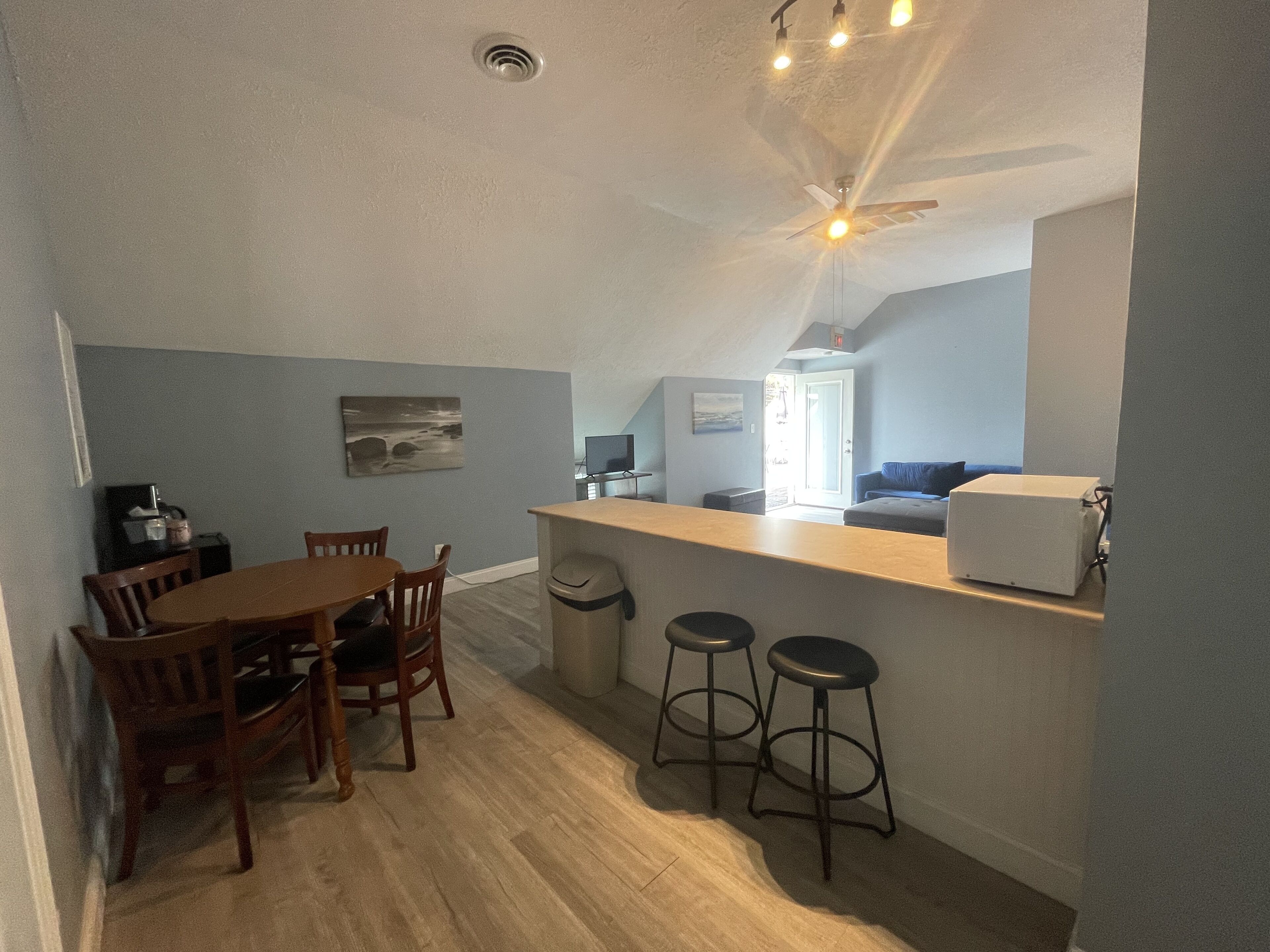 A compact kitchen with a dining area, wooden chairs, a small bar counter, and stools.