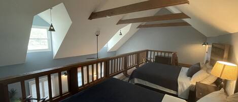 A bedroom with two beds, wooden beams, a skylight, and a nightstand with a lamp.