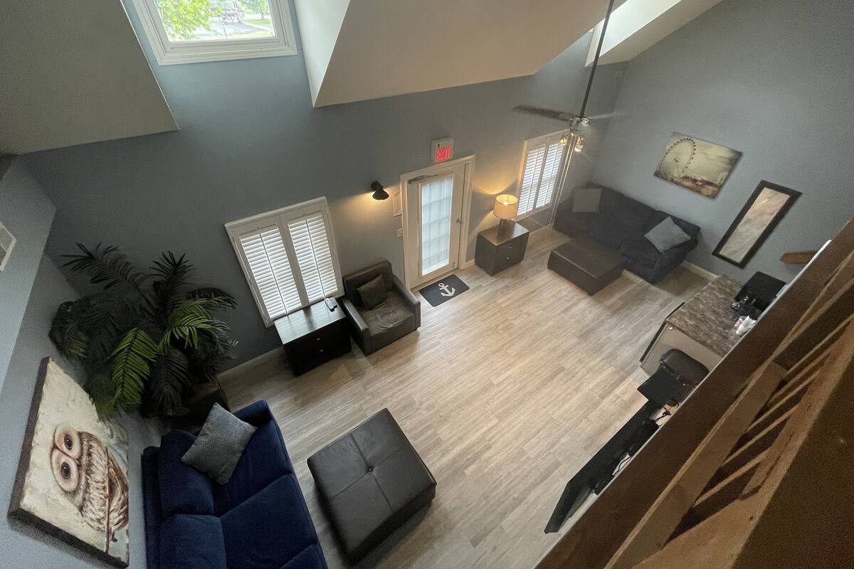 A spacious living area with a high ceiling, a ceiling fan, a dark blue sofa, a coffee table, and a dining table with chairs.