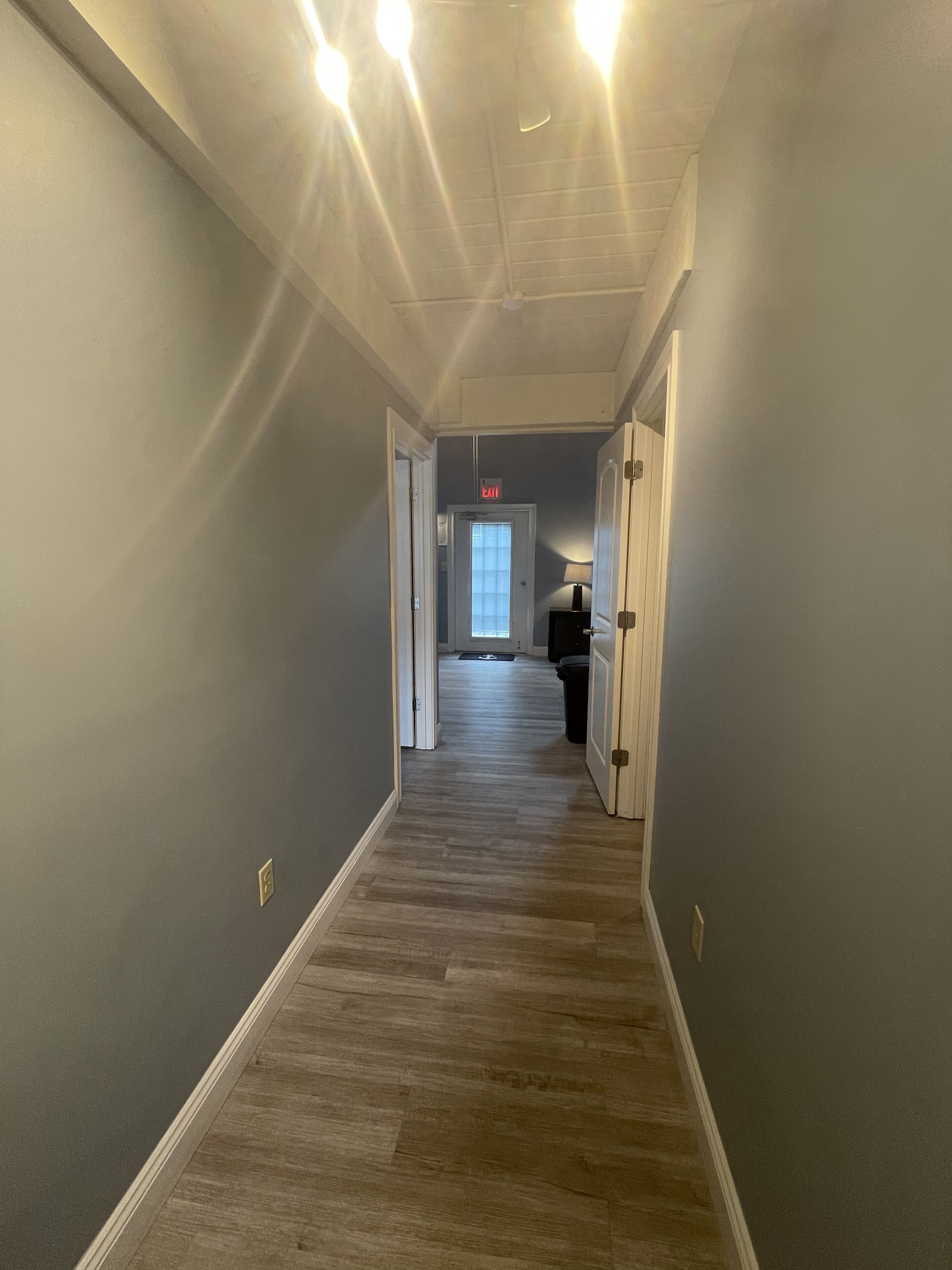 A hallway with a wooden floor, grey walls, and a door at the end.