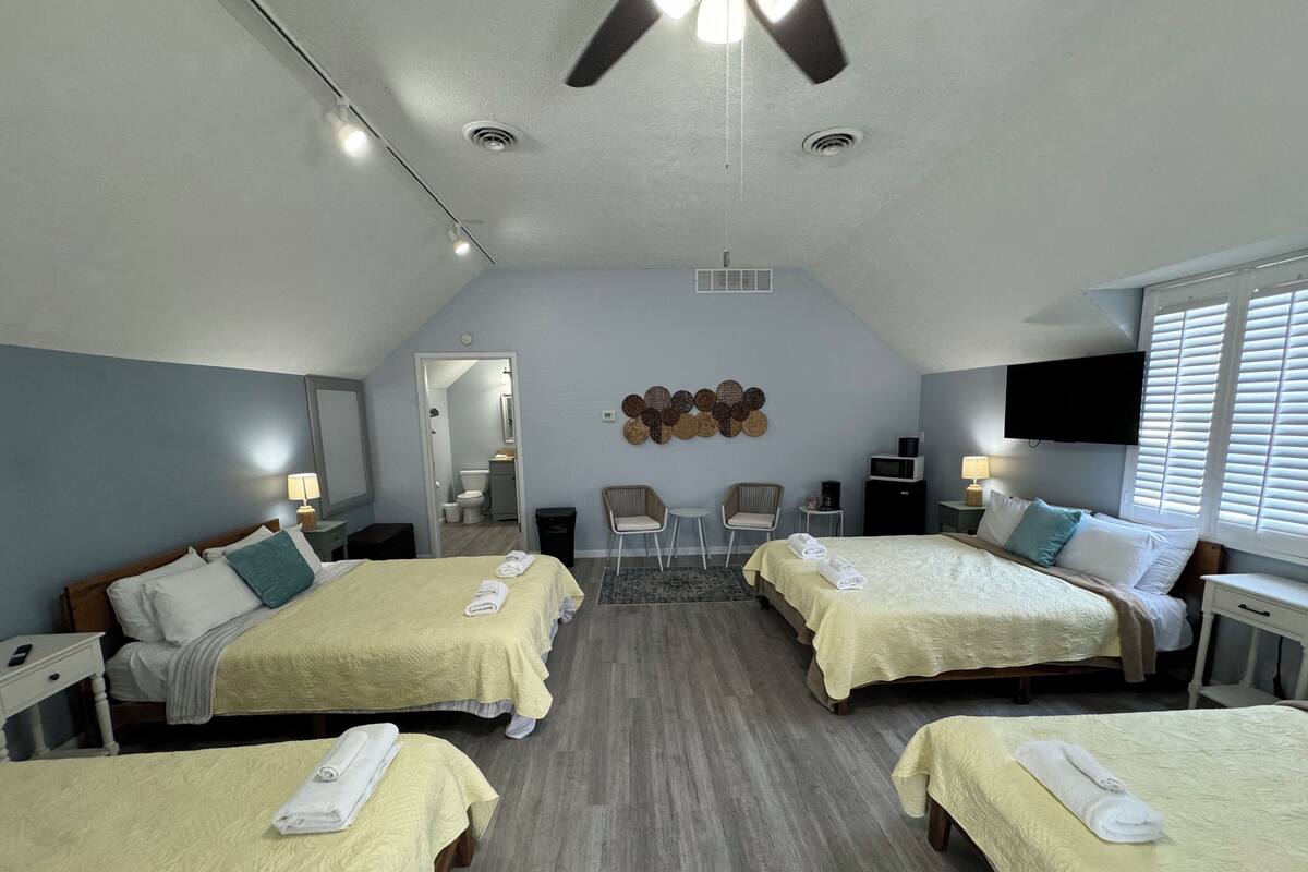 A hotel room with two beds, a ceiling fan, a TV, and a bathroom visible through an open door.