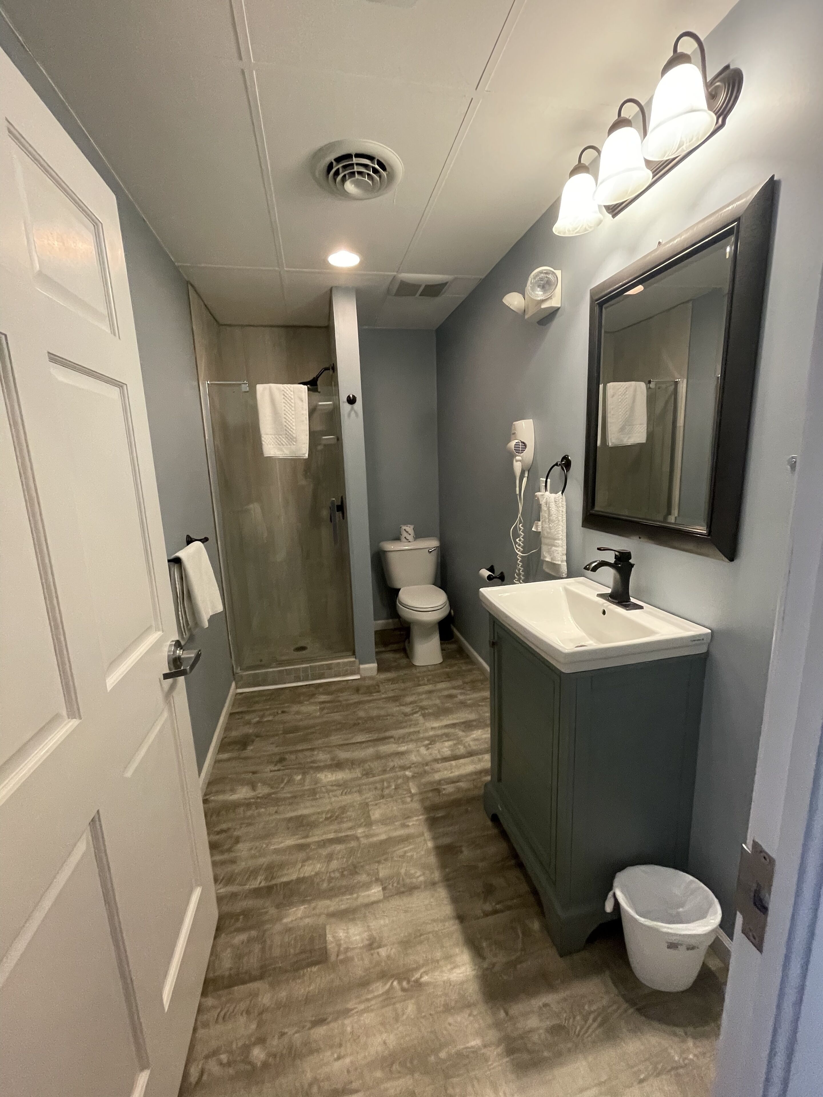 A bathroom with a shower, toilet, sink, and a mirror.