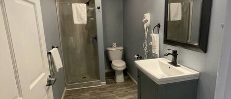 A bathroom with a shower, toilet, sink, and a mirror.