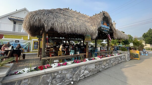 Un restaurante con techo de paja, mesas al aire libre y un muro de piedra adornado con flores.