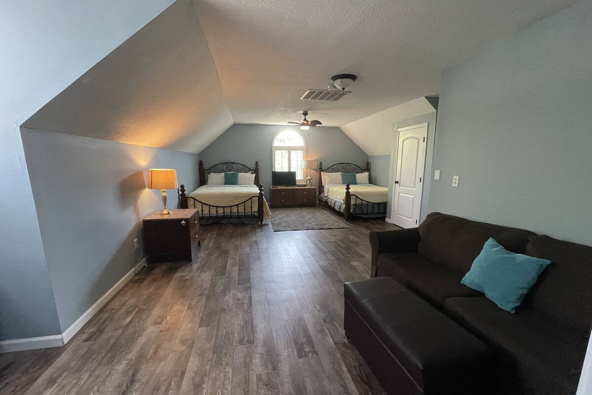 A bedroom with a loft-style ceiling, a bed, a nightstand, a dresser, a sofa, and a door.
