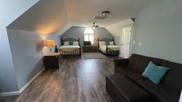 A bedroom with a loft-style ceiling, a bed, a nightstand, a dresser, a sofa, and a door.