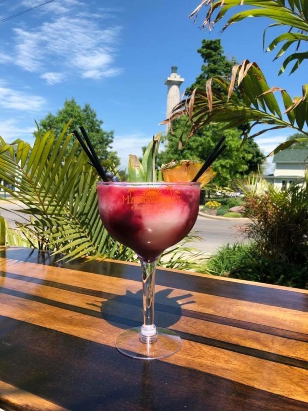 A cocktail glass with a straw on a wooden table outdoors.