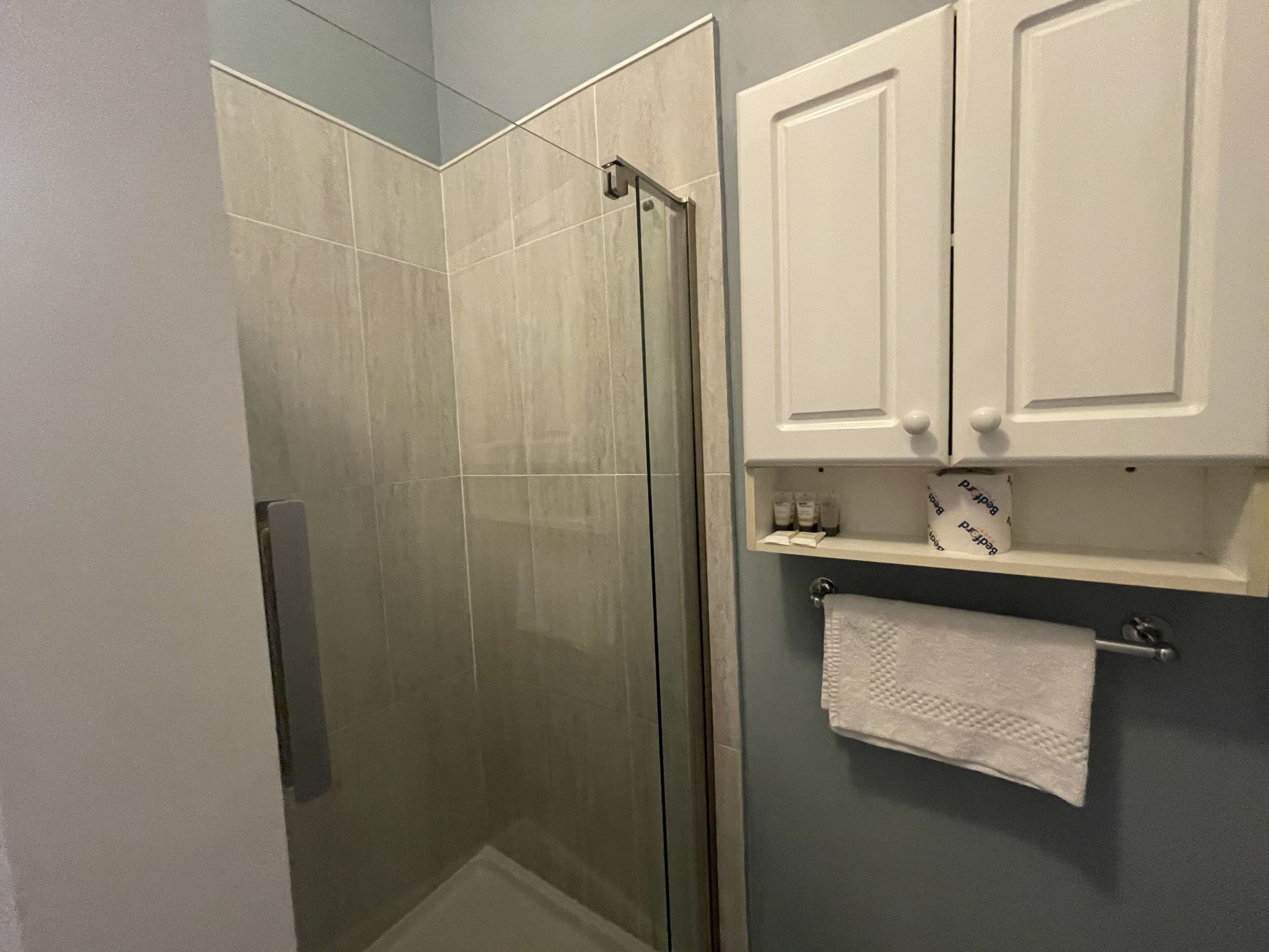 A bathroom with a glass shower door, white cabinets, and a towel rack.