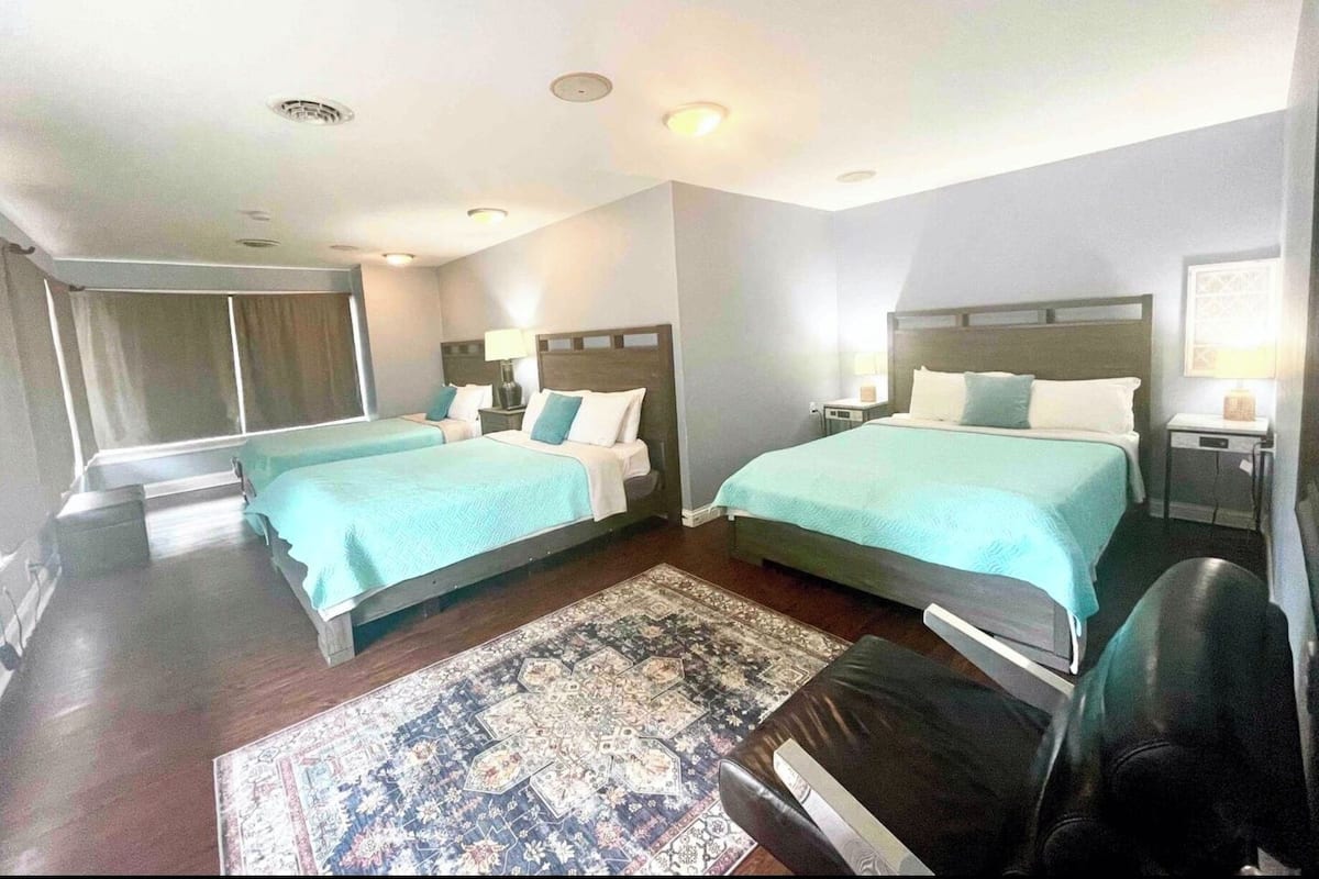 A hotel room with two beds, a large rug, and a view of the outdoors.