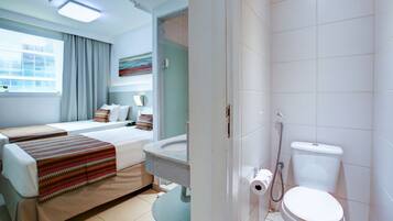Habitación de hotel con cama, baño con inodoro y ducha, y ventana con cortinas.