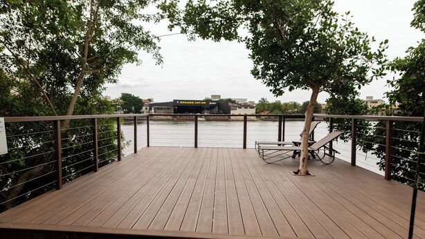 A wooden deck with metal railings, overlooking a river with buildings in the background. - Transamerica Fit Vitória Reta da Penha (Vitoria)