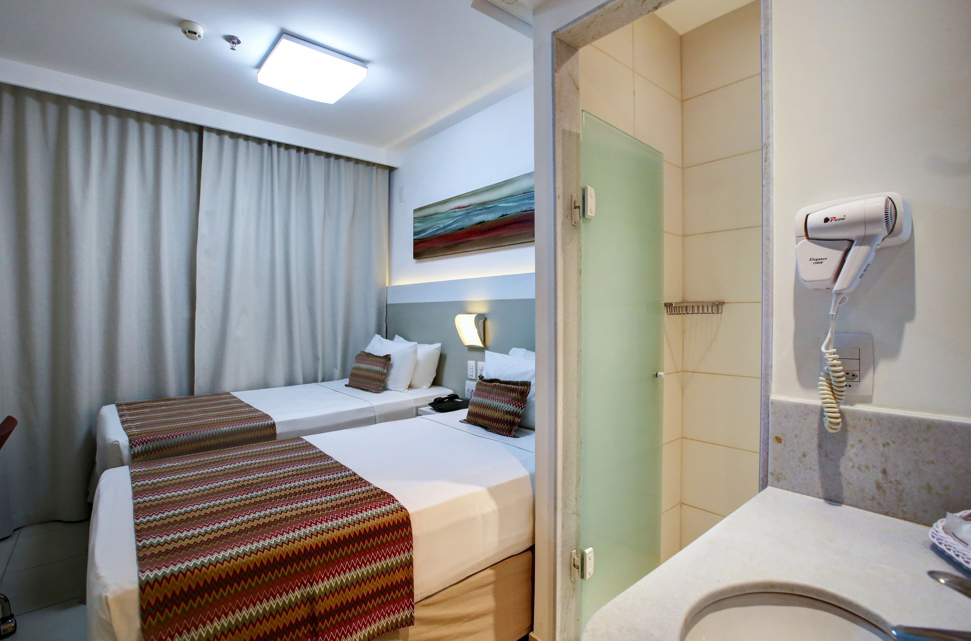 Ein Hotelzimmer mit zwei Betten, einem Badezimmer mit Fön und einem Bild an der Wand.