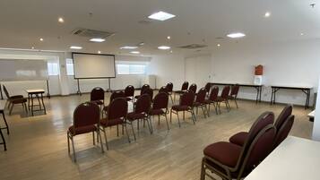 Un salón de conferencias con filas de sillas, una pizarra y una pantalla de proyector.