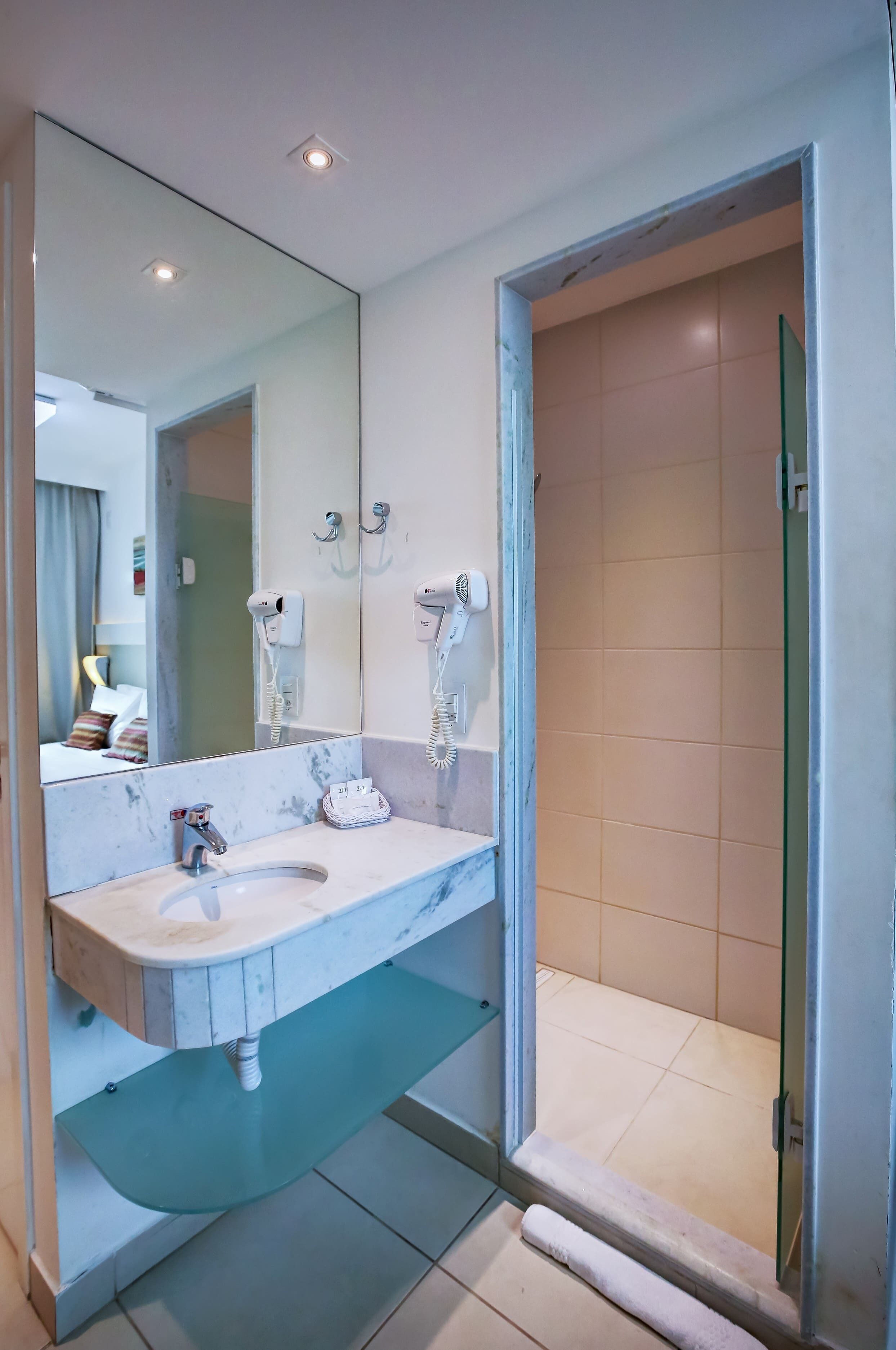 Un baño moderno con lavamanos de mármol, cabina de ducha con mampara de vidrio y un espejo grande.