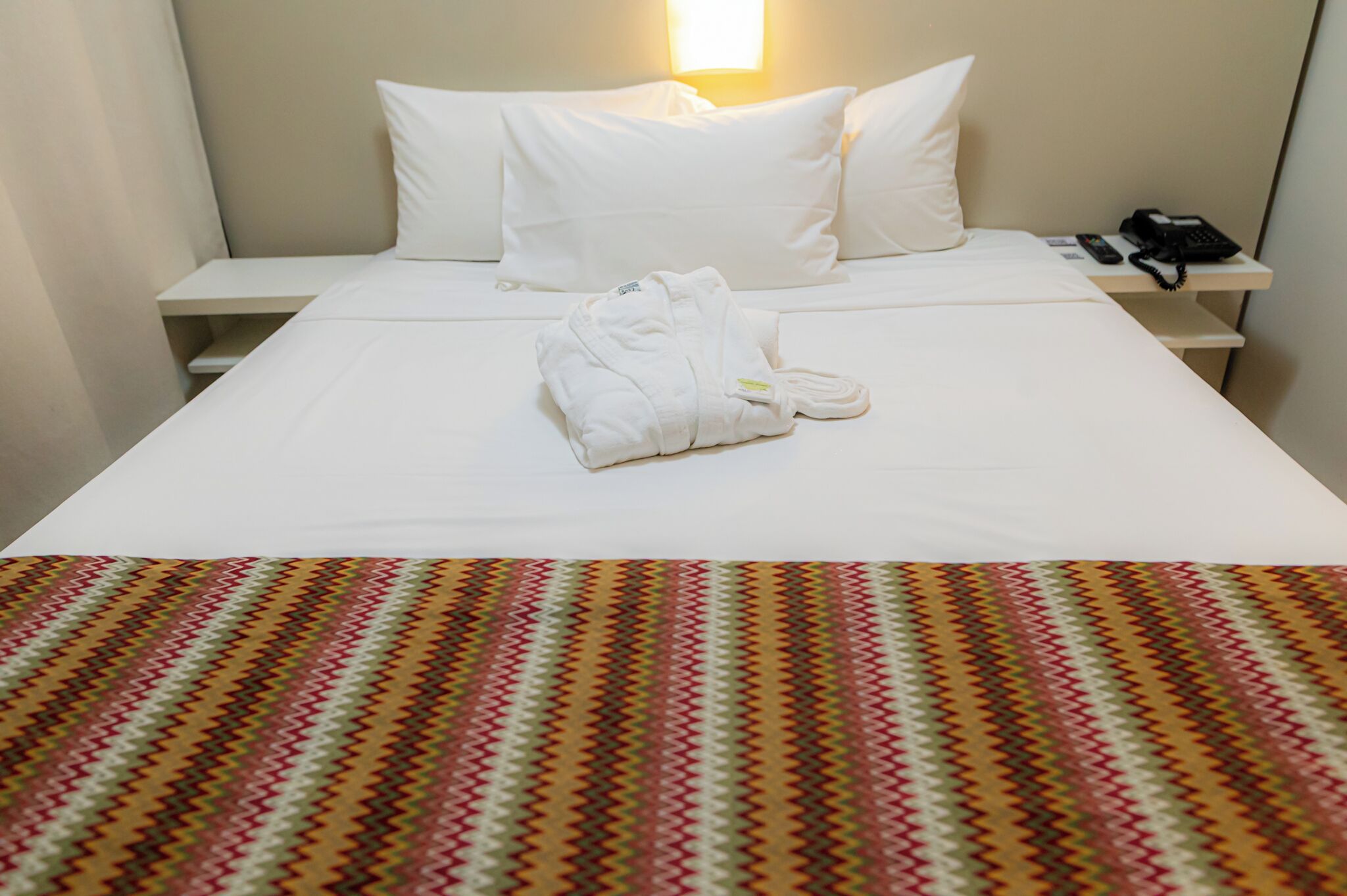 Una habitación de hotel con una cama bien hecha, un teléfono en la mesita de noche y una manta decorativa.