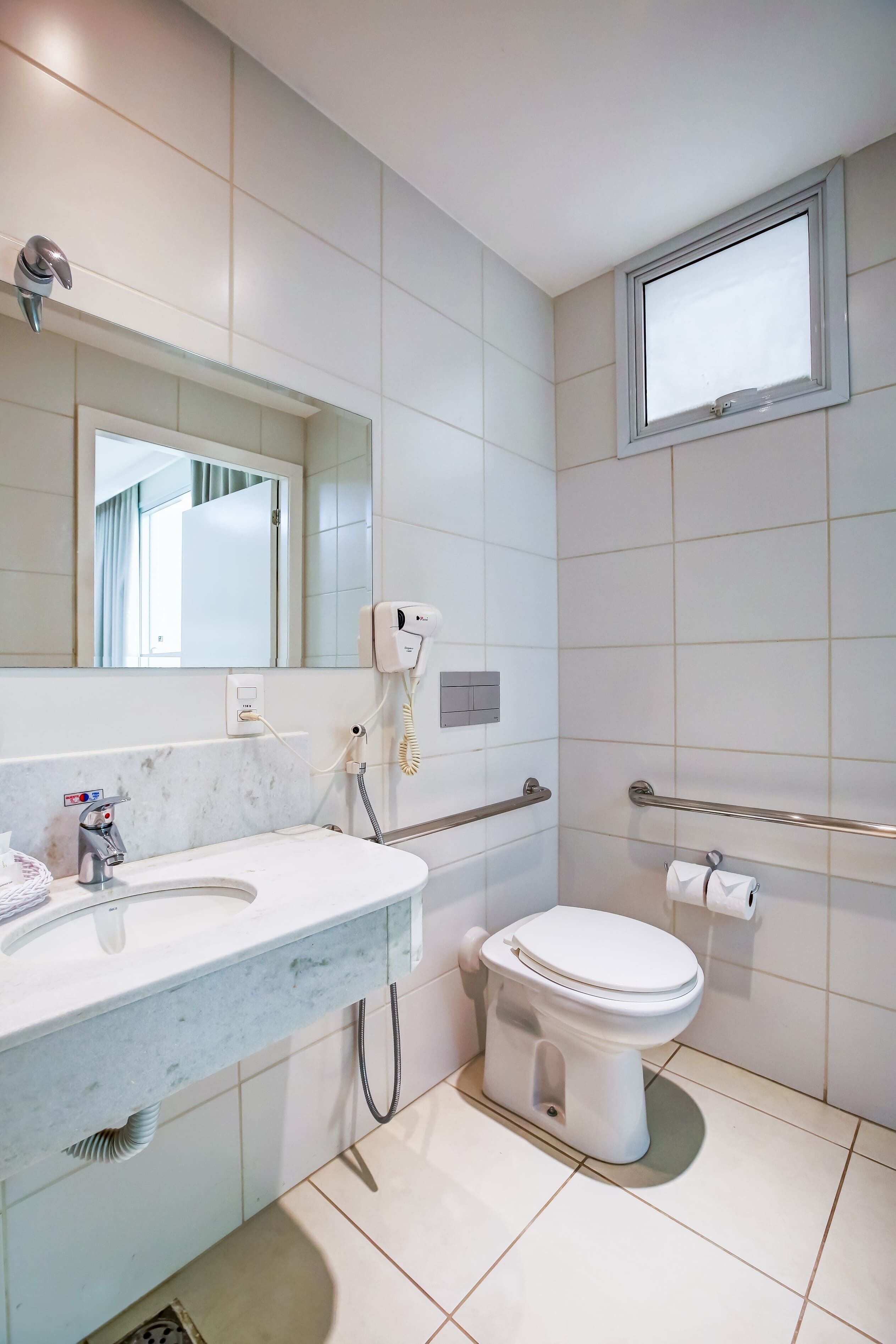 Une salle de bain moderne avec un lavabo en marbre, des toilettes, un sèche-cheveux et une fenêtre.