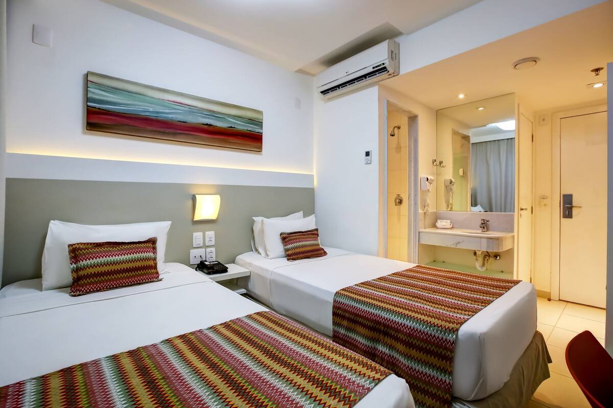Ein Hotelzimmer mit zwei Betten, einem Badezimmer mit Spiegel und einem roten Sessel.