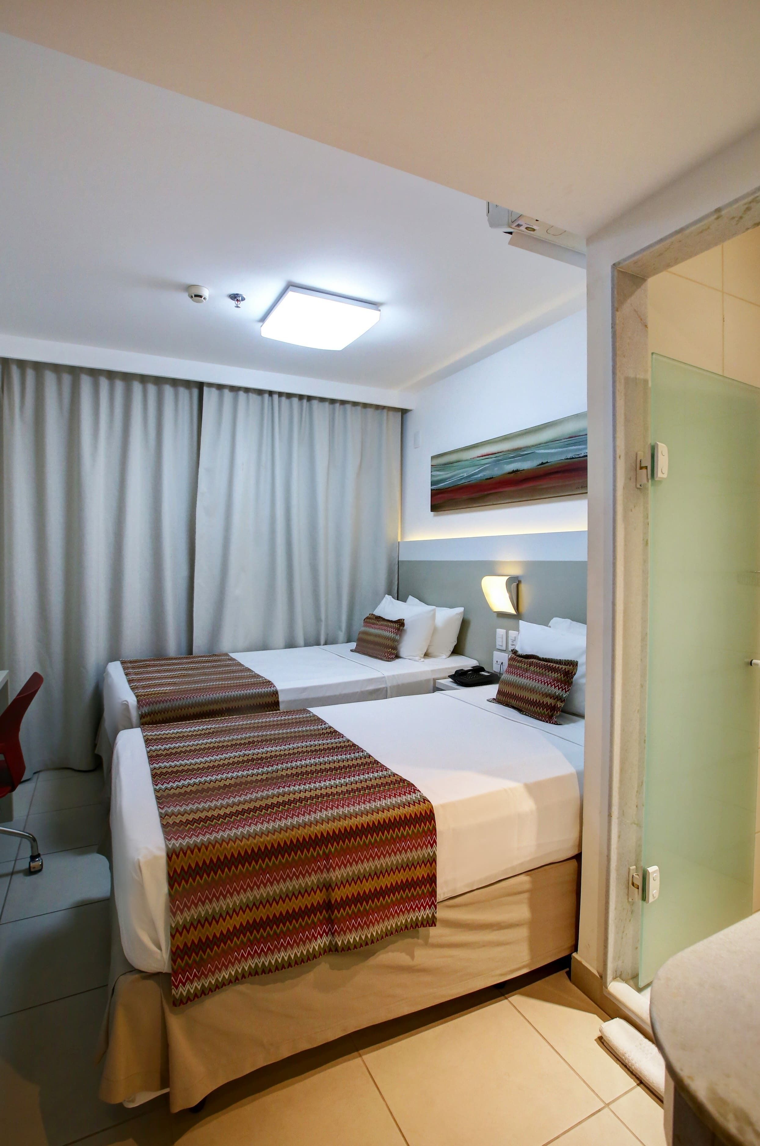 Habitación de hotel con dos camas, una lámpara en el techo, un cuadro y una puerta.