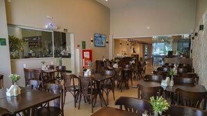 A spacious restaurant with multiple wooden tables and chairs, a coffee bar, and a large mirror on the wall. - Transamerica Fit Vitória Reta da Penha (Vitoria)