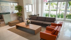 A modern hotel lobby with a reception desk, a sofa, a coffee table, and a view of the outside. - Transamerica Fit Vitória Reta da Penha (Vitoria)