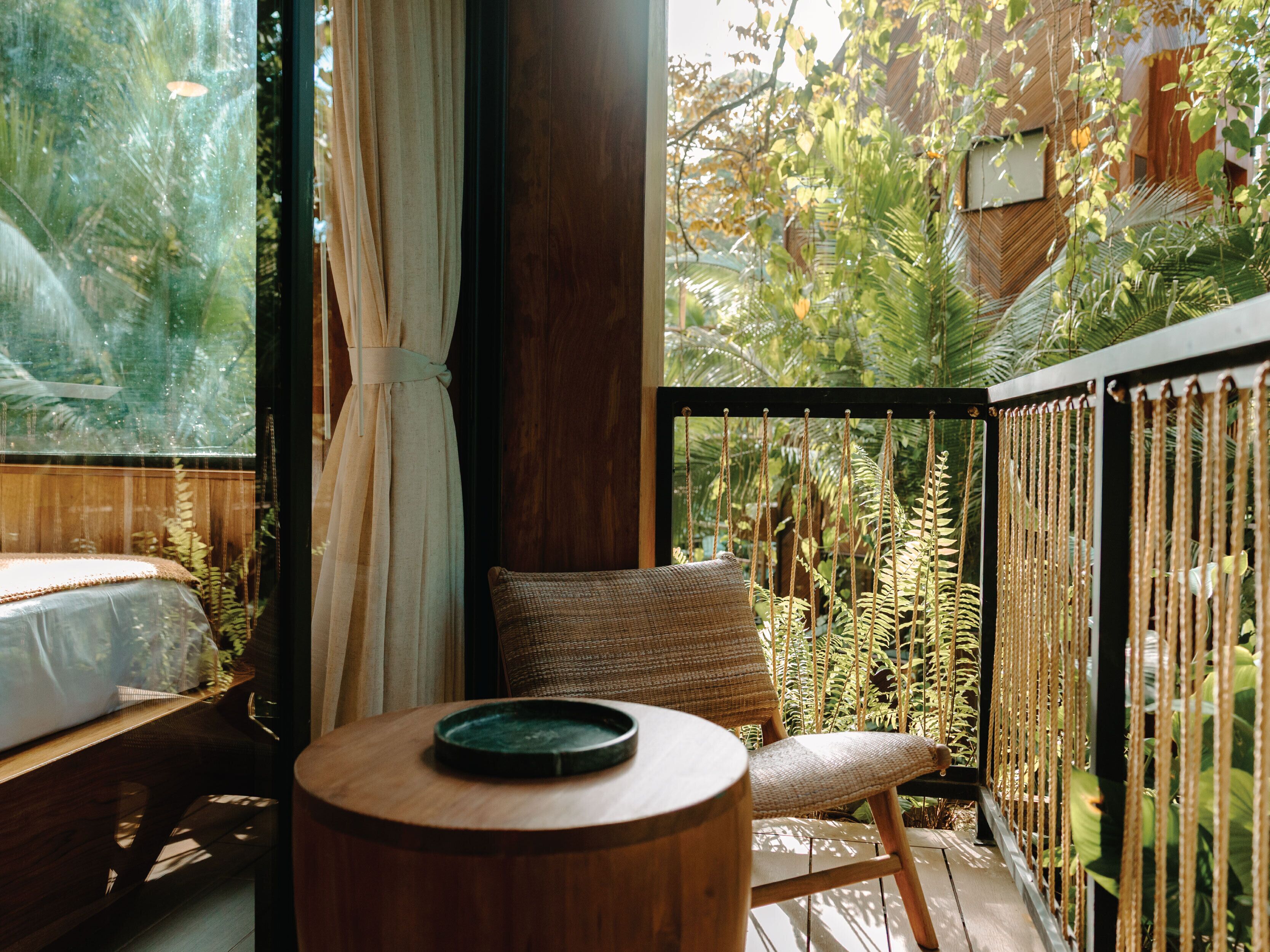 A room with a bed, a chair, a small table, and a view of a garden through a window.