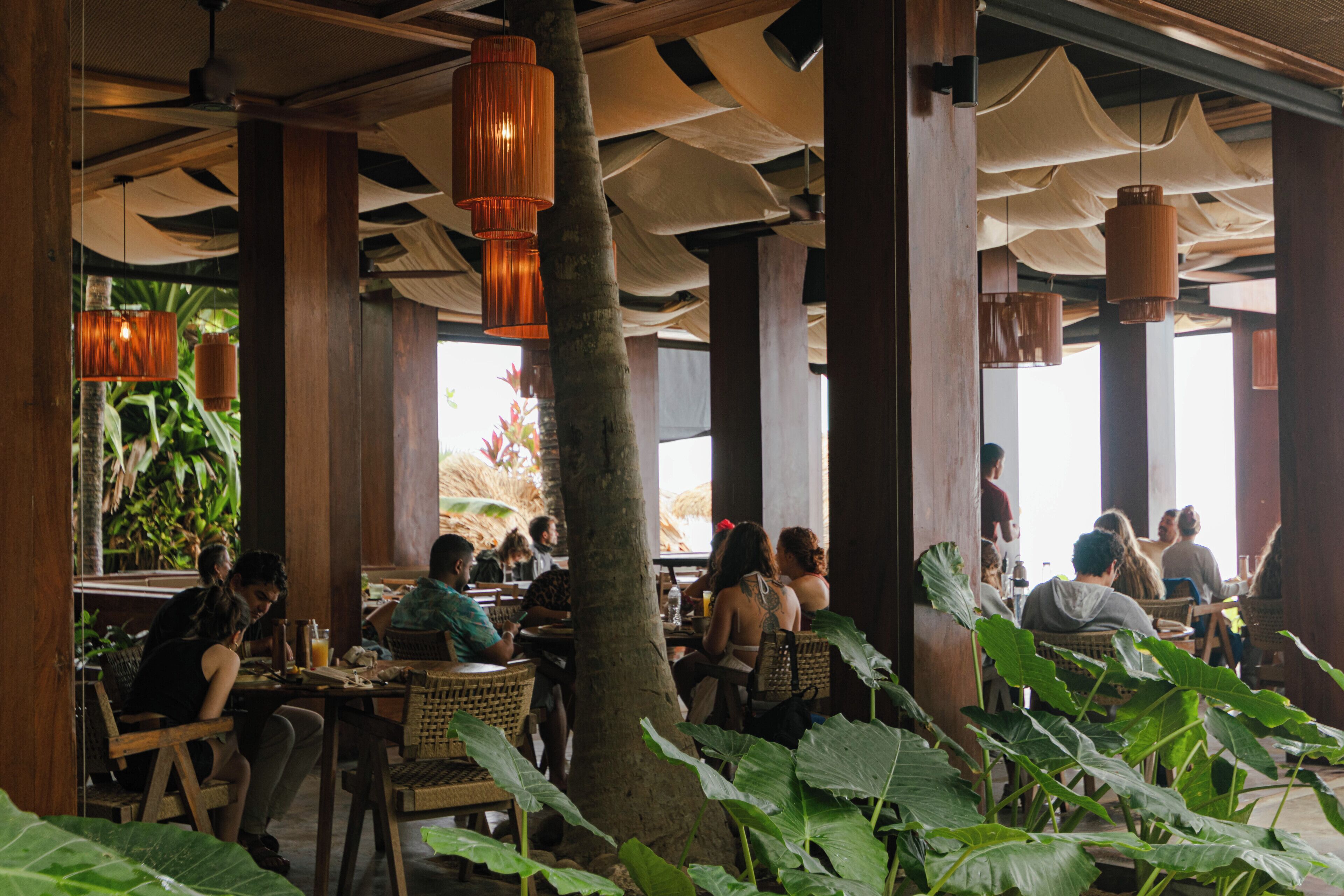 An indoor dining area with wooden pillars, woven chairs, and hanging lanterns.