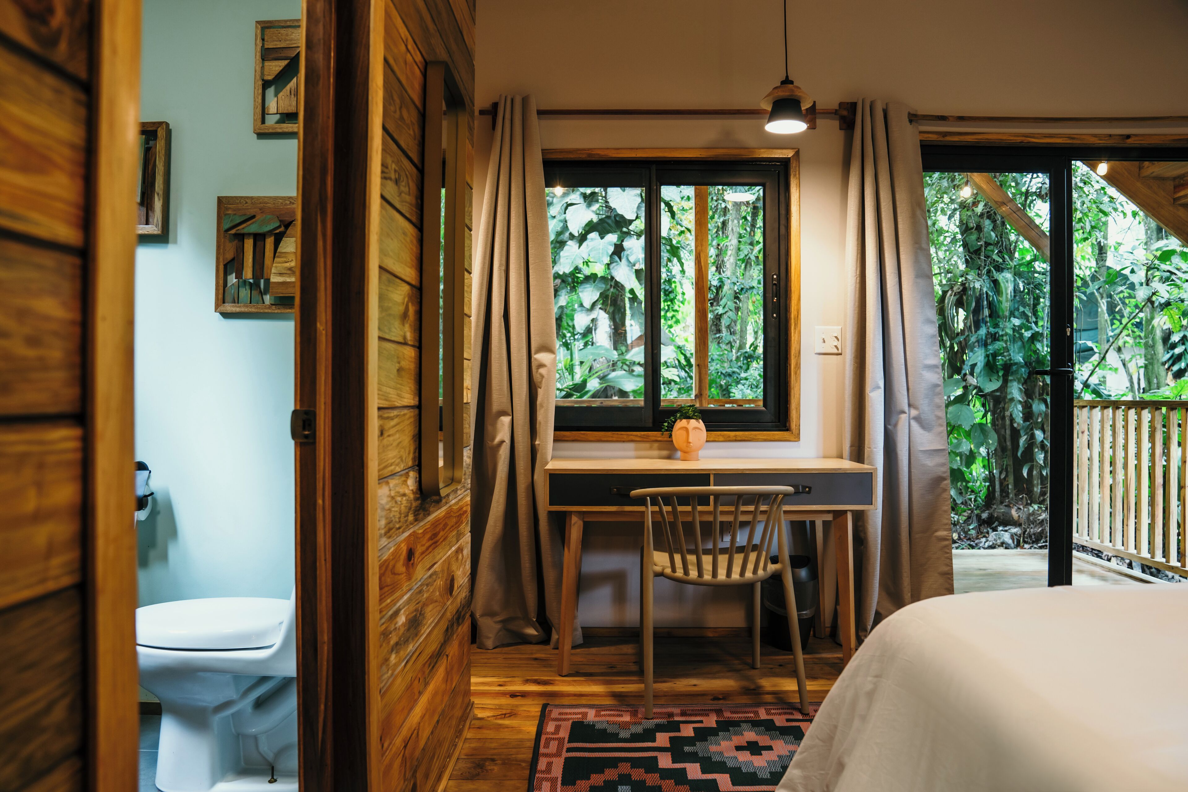 Una habitación con escritorio de madera, una silla, una cama y un ventanal con cortinas.