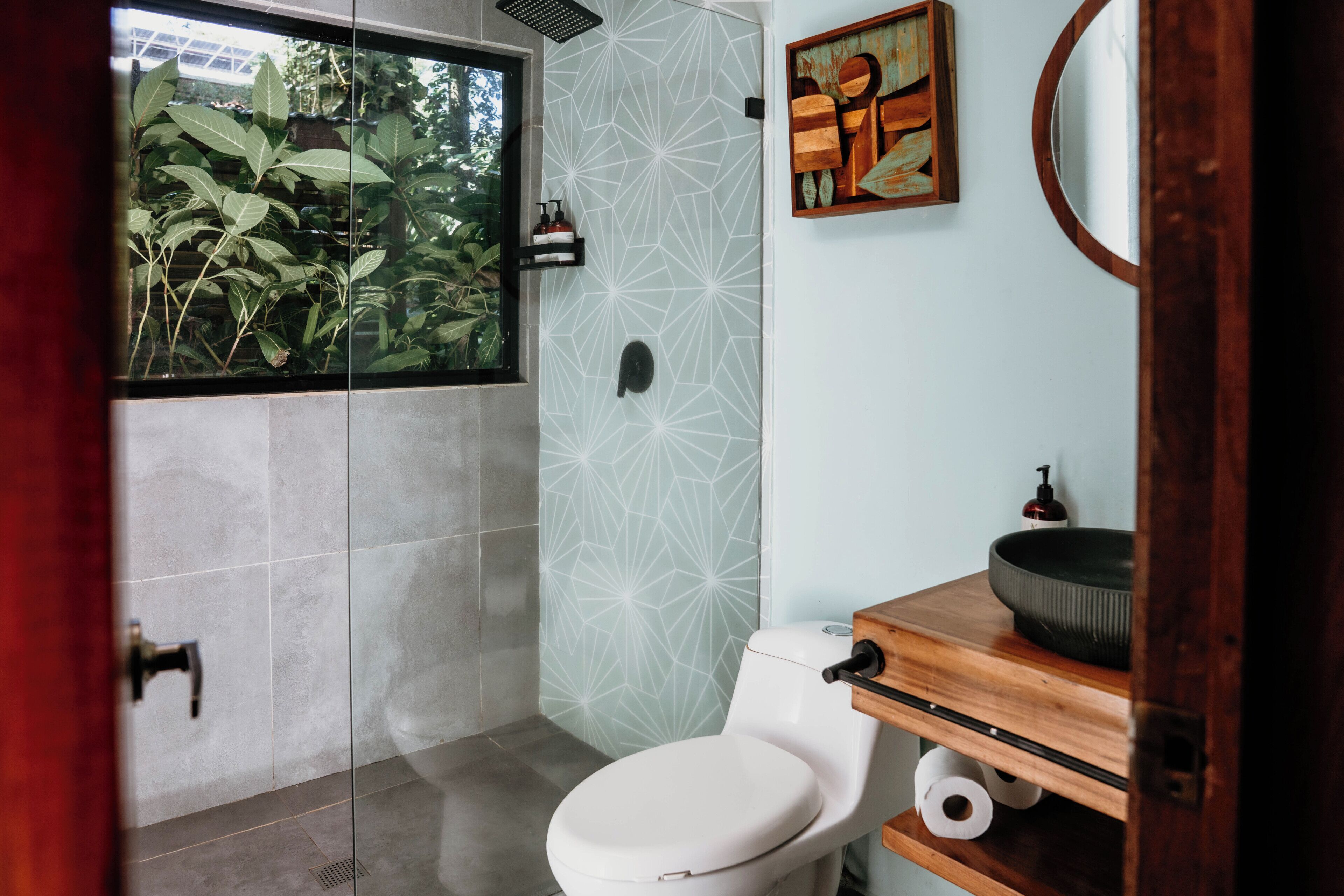Une salle de bain comprenant des toilettes, un lavabo, un miroir et une douche avec une porte en verre.