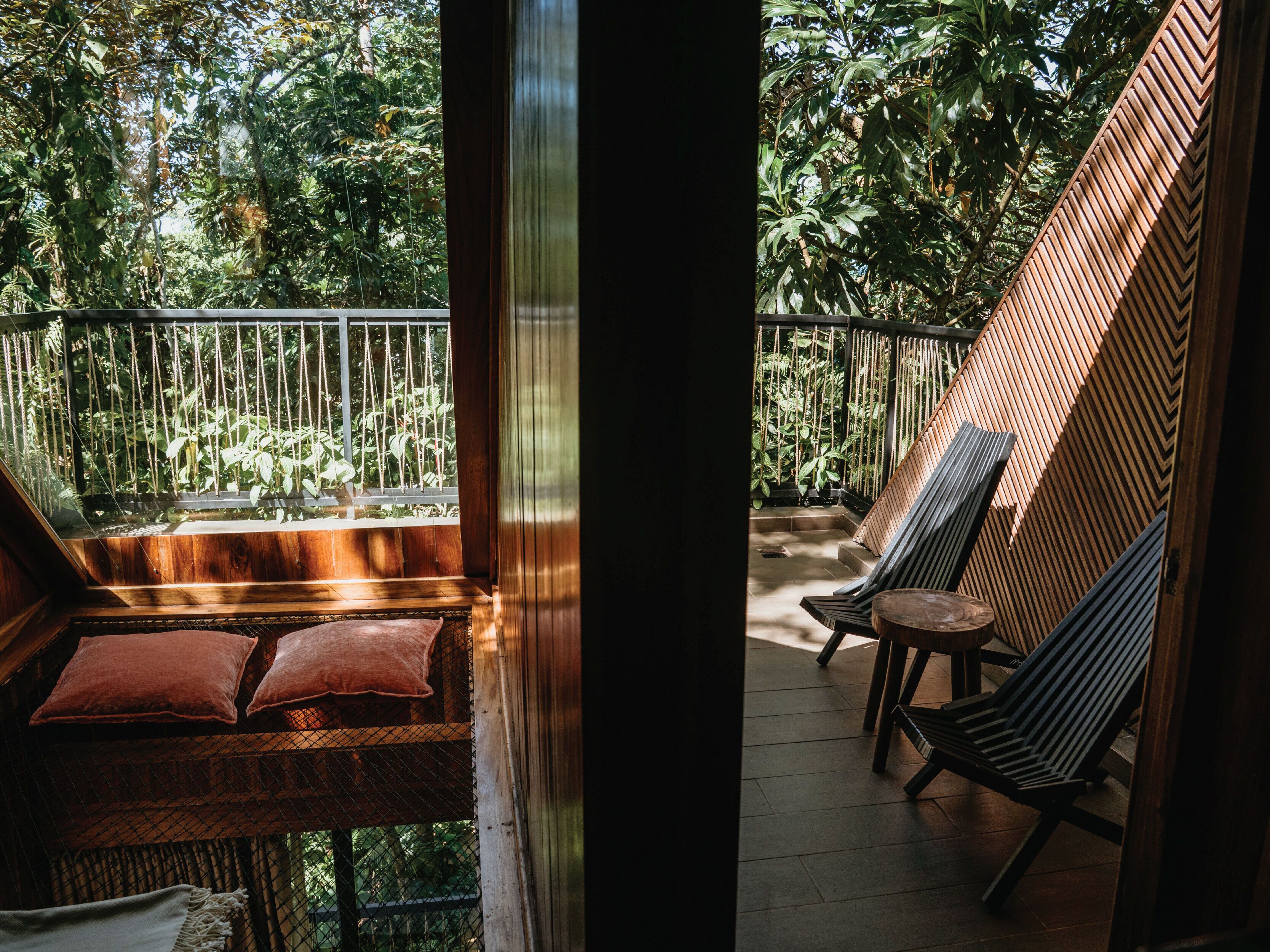 A wooden deck with a bench and chairs, surrounded by lush greenery.