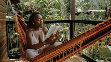 A person reading a book in a hammock on a wooden deck with lush greenery in the background.
