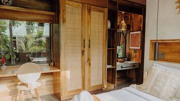 Una habitación de madera con una cama, un sillón de mimbre, un armario y una ventana con vistas a árboles.