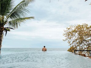 Un hombre en una piscina con vista al mar y una palmera.